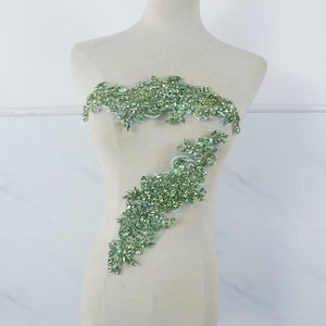 May include: Green beaded applique with a floral design. The applique is made of rhinestones and sequins and is attached to a mesh backing.