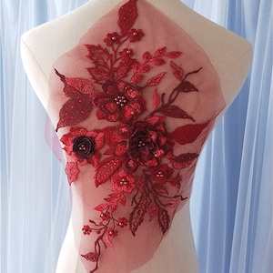 Peut inclure: Une application florale rouge foncé sur une base en maille transparente, avec des broderies complexes, des pétales en tissu superposés et de petites perles. Le motif comprend des feuilles et des fleurs détaillées dans des tons de rouge variés.