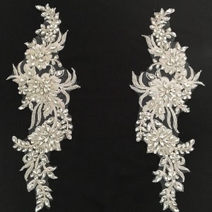 May include: Two silver beaded floral appliques with a delicate lace design. The appliques are perfect for adding a touch of sparkle and elegance to any project.