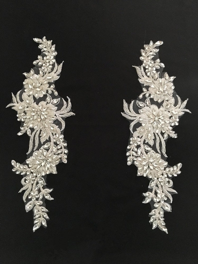 May include: Two silver beaded floral appliques with a delicate lace design. The appliques are perfect for adding a touch of sparkle and elegance to any project.