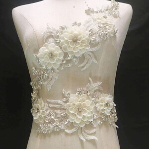 May include: White floral applique with silver beading and sequins. This delicate lace trim is perfect for adding a touch of elegance to wedding dresses, bridal gowns, and other special occasion garments.