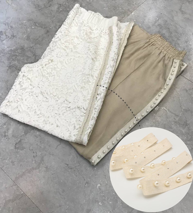 May include: Two pairs of pants, one white lace and one beige with pearl trim. A close-up of beige trim with pearls.