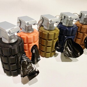 May include: A collection of five dog waste bag dispensers shaped like hand grenades. Each dispenser is a different color: black, coral, olive green, navy blue, and brown. The top and pull pin are silver, and a black bag is visible in the opening.