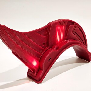 Op de afbeelding: Een rode helm van 3D-geprint plastic met een gebogen ontwerp en een licht erin.