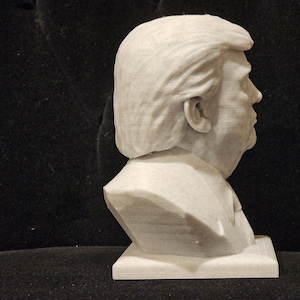 May include: A white bust sculpture of a person with short, wavy hair. The sculpture is on a white base and is viewed from the side.