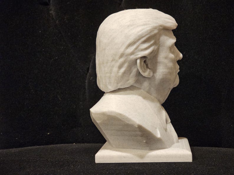 May include: A white bust sculpture of a person with short, wavy hair. The sculpture is on a white base and is viewed from the side.