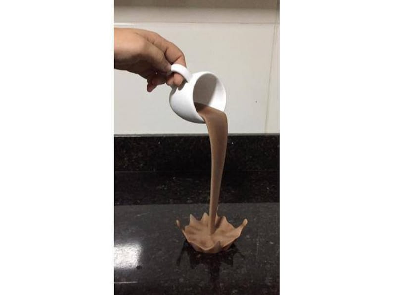 May include: A white ceramic mug pouring brown liquid into a puddle on a black countertop.