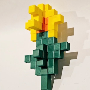 May include: A 3D printed flower made of green and yellow blocks. The flower has a yellow centre and green stem.