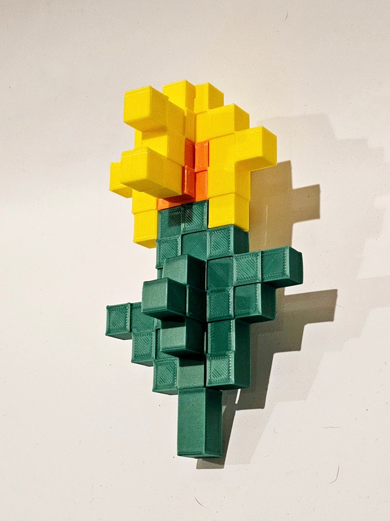 May include: A 3D printed flower made of green and yellow blocks. The flower has a yellow centre and green stem.