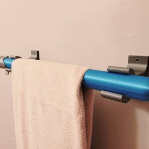 May include: A blue towel bar with silver brackets mounted on a white wall. A white towel is hanging on the bar.