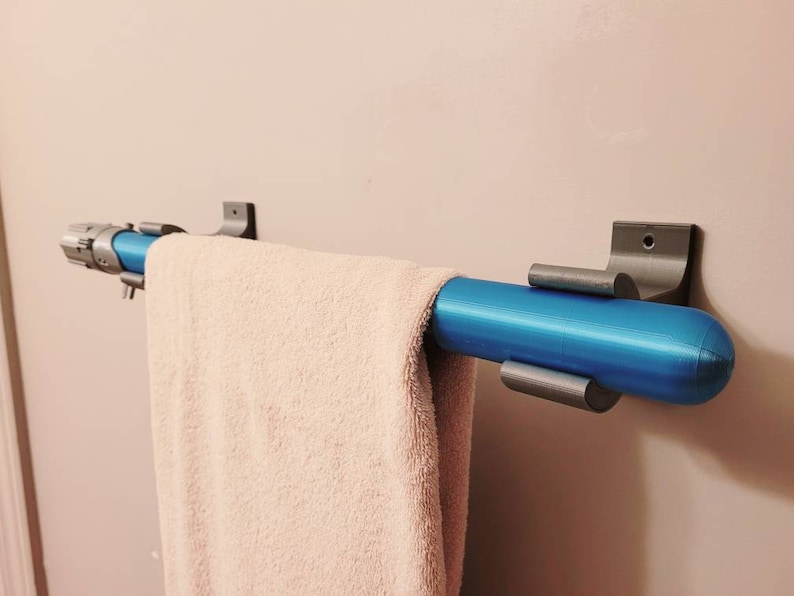 May include: A blue towel bar with silver brackets mounted on a white wall. A white towel is hanging on the bar.