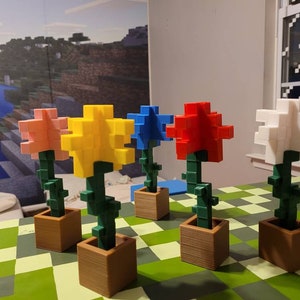 May include: Five colourful flower arrangements made of plastic blocks in brown pots. The flowers are pink, yellow, blue, red, and white. The pots are sitting on a green and white chequered surface.