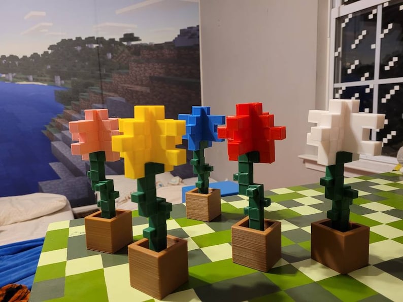May include: Five colourful flower arrangements made of plastic blocks in brown pots. The flowers are pink, yellow, blue, red, and white. The pots are sitting on a green and white chequered surface.