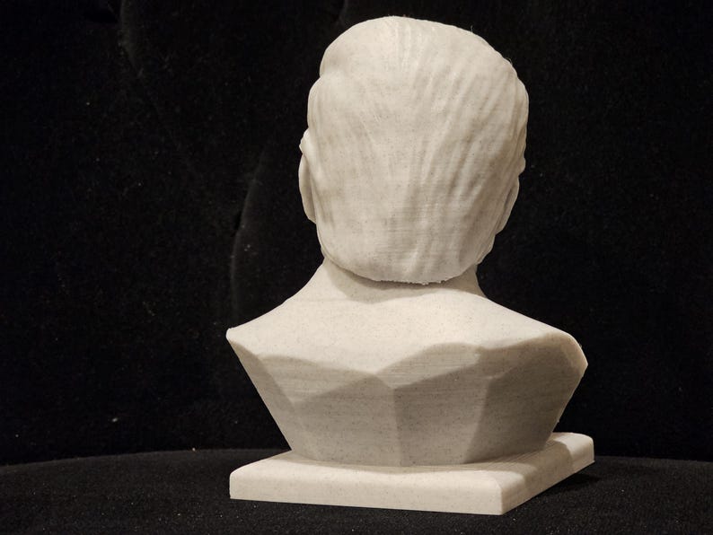 May include: White plaster bust sculpture of a person's head and shoulders. The bust is on a white base.