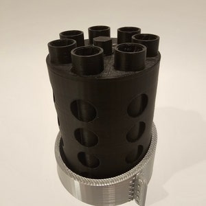 May include: A black 3D printed cylinder with six round openings on top and a silver 3D printed base.