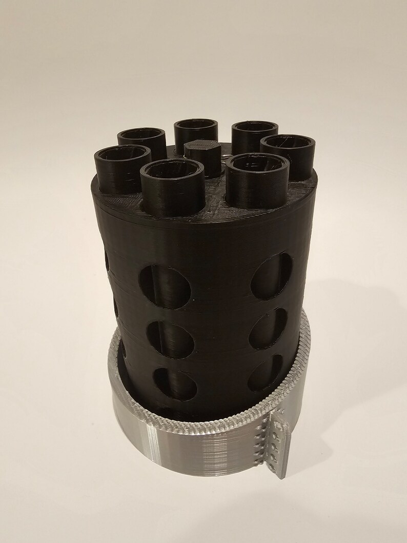 May include: A black 3D printed cylinder with six round openings on top and a silver 3D printed base.