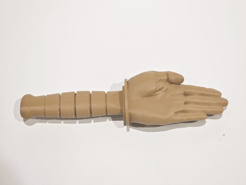 May include: A tan-colored, 3D printed hand with a segmented arm. The hand is open and the fingers are spread apart. The arm is segmented into several sections, giving it a textured appearance.