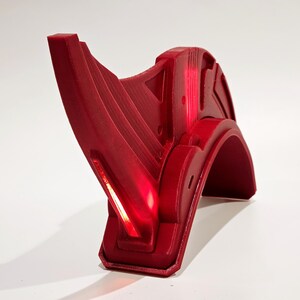 Op de afbeelding: Een rode plastic helm met een puntig, hoekig ontwerp. De helm heeft een licht dat rood gloeit.