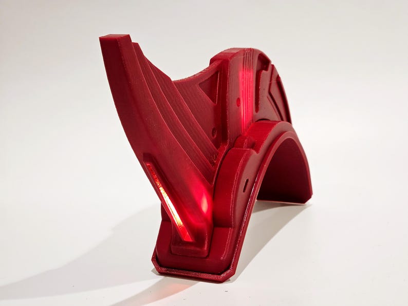Op de afbeelding: Een rode plastic helm met een puntig, hoekig ontwerp. De helm heeft een licht dat rood gloeit.