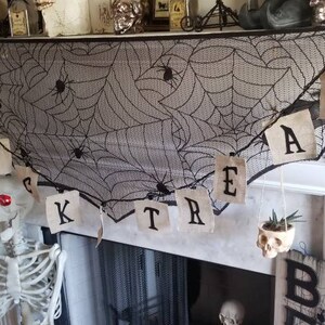 May include: A black and white spiderweb garland with the word "TREAT" written on it hangs above a fireplace. A small succulent plant is in a skull planter. Two skeletons are sitting on the hearth. A black pumpkin with holes in it is on the floor. A sign that says "BEWARE" is on the right side of the fireplace.