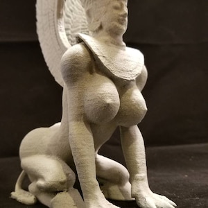 May include: White 3D printed figurine of a woman with wings, a crown, and a necklace. She is kneeling with her hands on the ground.