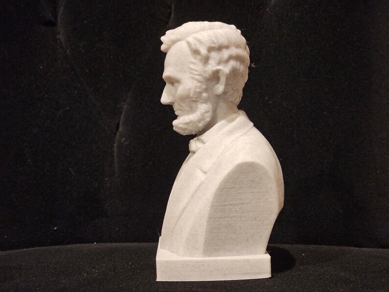 May include: A white bust sculpture of a man with a beard and short hair. The sculpture is on a white base.