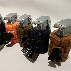 May include: A row of five dog waste bag dispensers shaped like grenades. Each dispenser is a different color: black, orange, olive green, navy blue, and brown. The top of each dispenser is silver, and a black bag is visible.