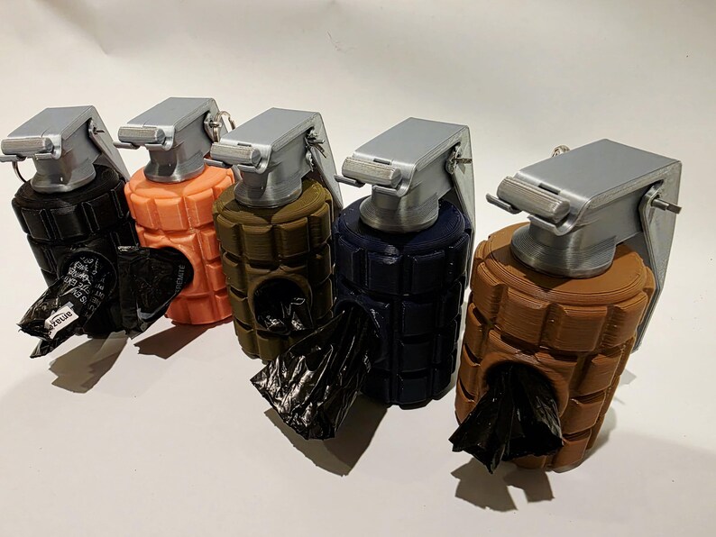 May include: A row of five dog waste bag dispensers shaped like grenades. Each dispenser is a different color: black, orange, olive green, navy blue, and brown. The top of each dispenser is silver, and a black bag is visible.