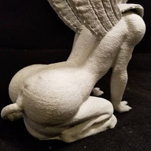 May include: A white, detailed, gargoyle statue with wings, sitting on its haunches. The statue is made of a textured material and has a realistic appearance.