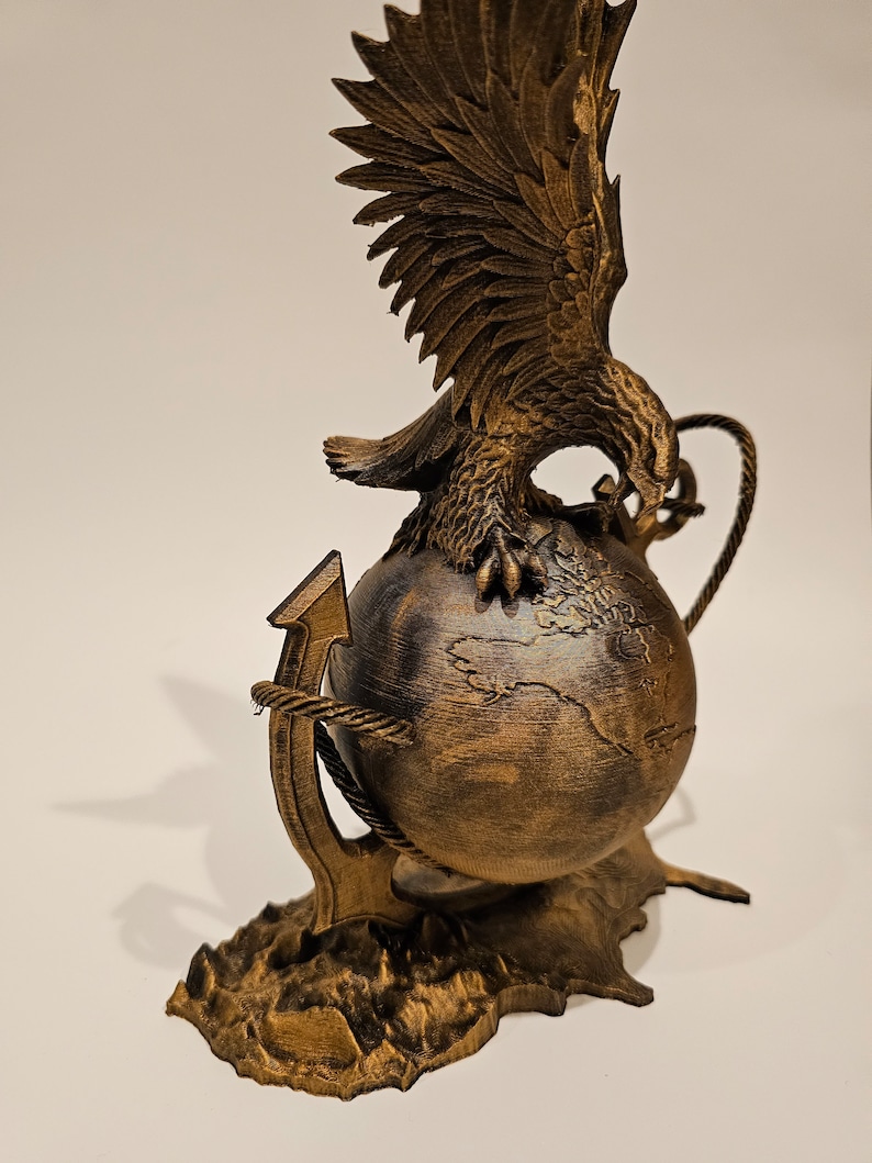 May include: A gold-colored eagle sculpture with outstretched wings perched on a globe, anchored by a rope-wrapped anchor. The globe has a detailed map of the world.