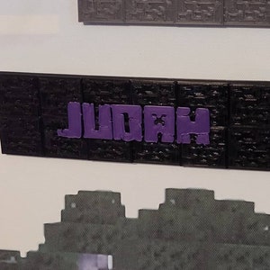 Pode incluir: Uma placa impressa em 3D preta e roxa com a palavra "JUDAH" em letras roxas.
