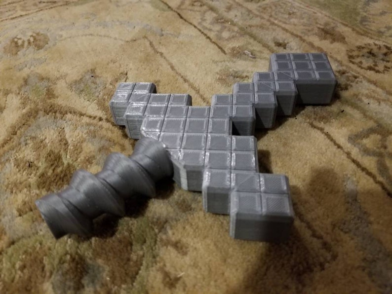Op de afbeelding: Een grijs 3D-geprint Minecraft-zwaard met een draaiende handvat.