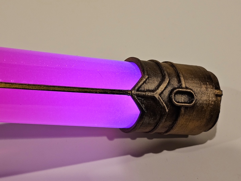 May include: A close-up of a purple glowing tube with a brown metal cap. The cap has a decorative design and a small oval opening.