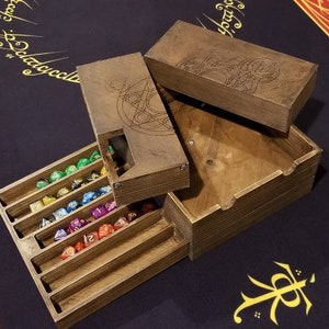 May include: A wooden dice box with a compartment for storing dice. The box has a lid with an engraved design. The box is open and the dice are visible. The dice are multi-colored.