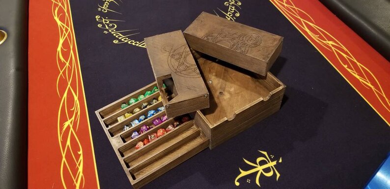 May include: A wooden dice box with a compartment for storing dice. The box has a lid with an engraved design. The box is open and the dice are visible. The dice are multi-colored.