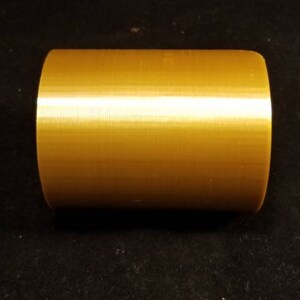 May include: A solid gold-colored cylinder with a smooth, slightly textured surface.