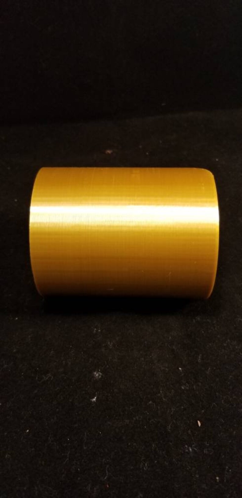 May include: A solid gold-colored cylinder with a smooth, slightly textured surface.