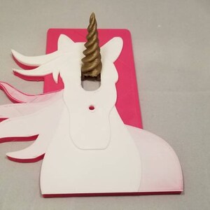 May include: A pink and white unicorn light switch cover with a gold horn. The unicorn's mane is flowing in the wind.