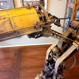 Puede incluir: Una l&aacute;mpara de estilo steampunk con una base de metal amarilla y engranajes y palancas intrincados. La l&aacute;mpara est&aacute; hecha de madera y metal y tiene un aspecto r&uacute;stico e industrial.