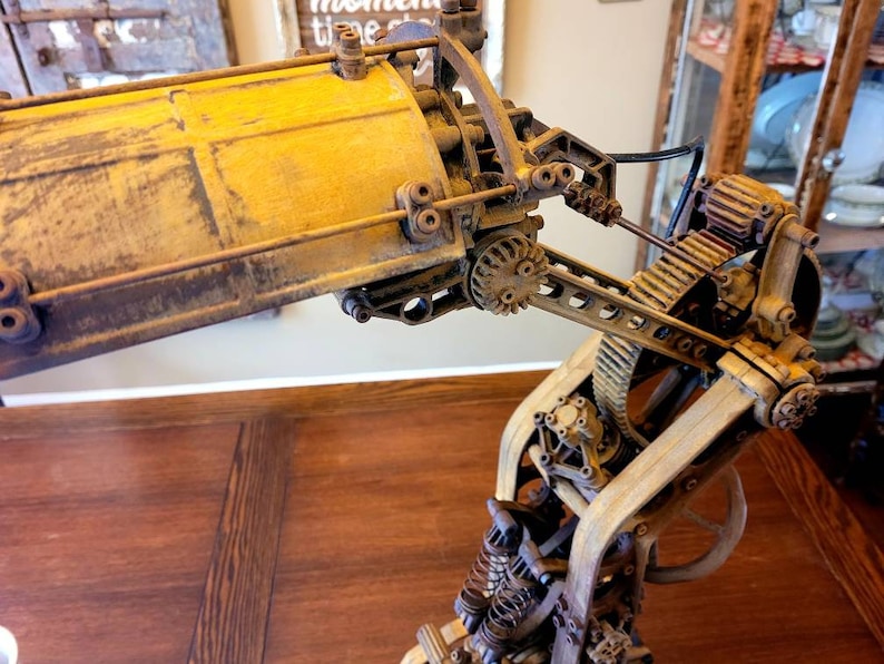 Puede incluir: Una l&aacute;mpara de estilo steampunk con una base de metal amarilla y engranajes y palancas intrincados. La l&aacute;mpara est&aacute; hecha de madera y metal y tiene un aspecto r&uacute;stico e industrial.