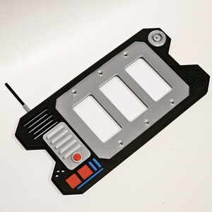 May include: A black and silver handheld device with a rectangular shape and a silver panel with three rectangular openings. The device has a red button and a blue and red stripe design.