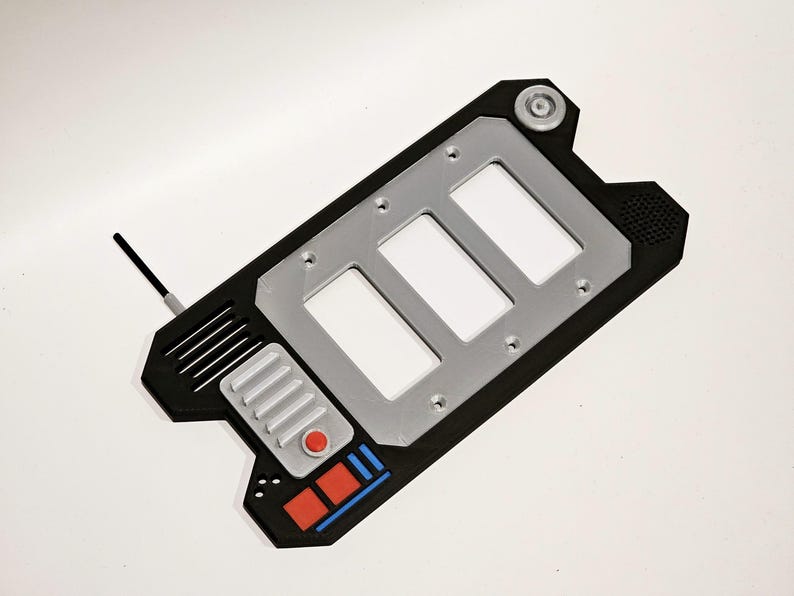 May include: A black and silver handheld device with a rectangular shape and a silver panel with three rectangular openings. The device has a red button and a blue and red stripe design.