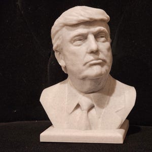 May include: A white marble bust sculpture of a person with short, combed-back hair. The sculpture is on a white marble base.
