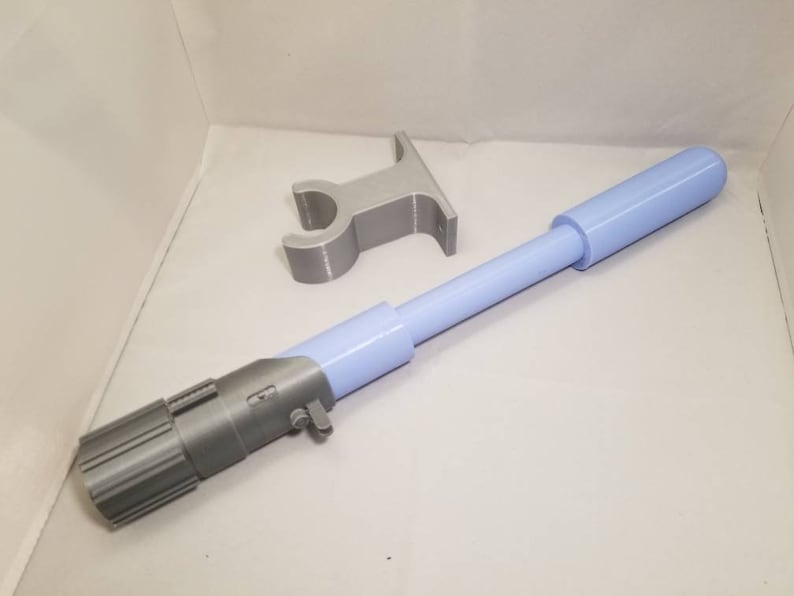 May include: A light blue and gray 3D-printed prop, resembling a lightsaber, with a cylindrical body and detailed handle. A separate gray stand is also present. The prop is designed with a focus on detail and a futuristic aesthetic.