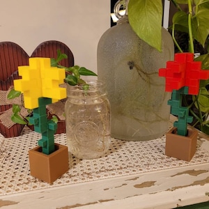 May include: Two small potted plants with pixelated flowers. The plant on the left has a yellow flower and the plant on the right has a red flower. Both plants are in brown pots.
