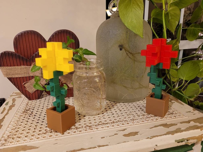 May include: Two small potted plants with pixelated flowers. The plant on the left has a yellow flower and the plant on the right has a red flower. Both plants are in brown pots.