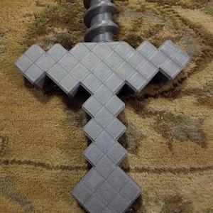 Op de afbeelding: Een grijs 3D-geprint Minecraft-zwaard met een pixelontwerp. Het zwaard heeft een spiraalvormige handgreep.