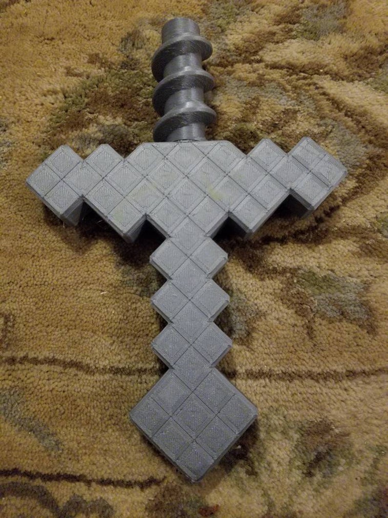 Op de afbeelding: Een grijs 3D-geprint Minecraft-zwaard met een pixelontwerp. Het zwaard heeft een spiraalvormige handgreep.
