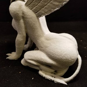 May include: A white, detailed, gargoyle statue with wings, sitting on its haunches. The gargoyle has a long tail and a textured surface.