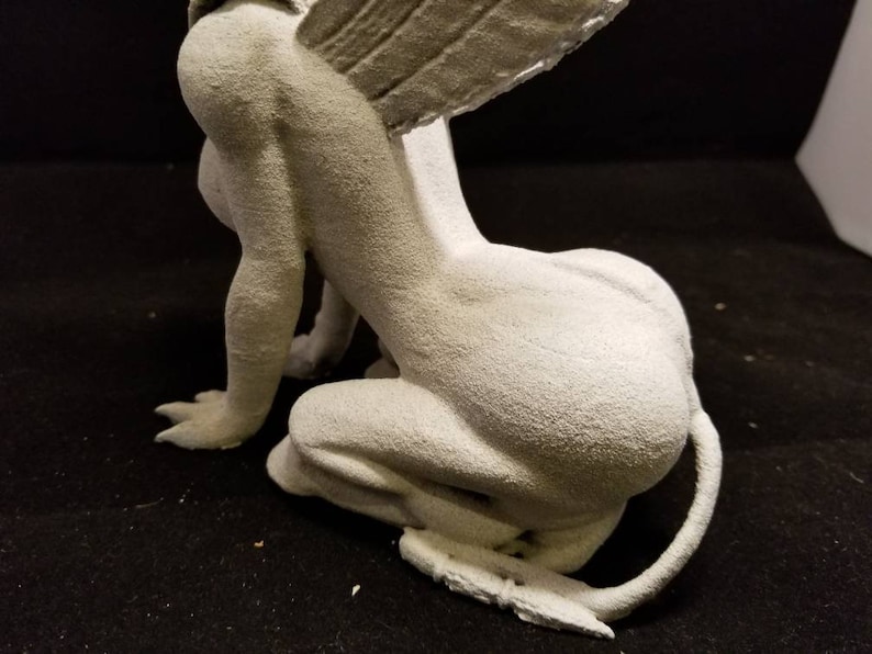 May include: A white, detailed, gargoyle statue with wings, sitting on its haunches. The gargoyle has a long tail and a textured surface.